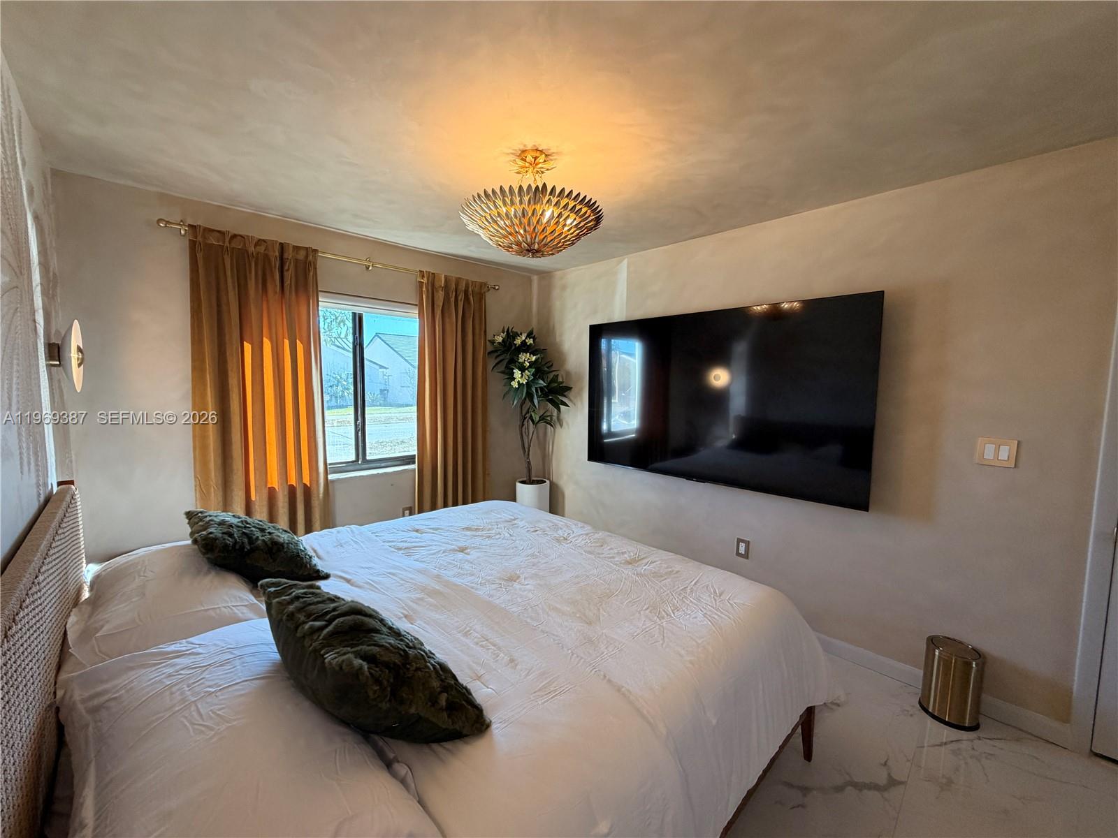 A bedroom features a wall-mounted television, a bed with green pillows, and gold curtains — 14617 SW 167th Ter, Miami FL 33177, MIAMI, FL