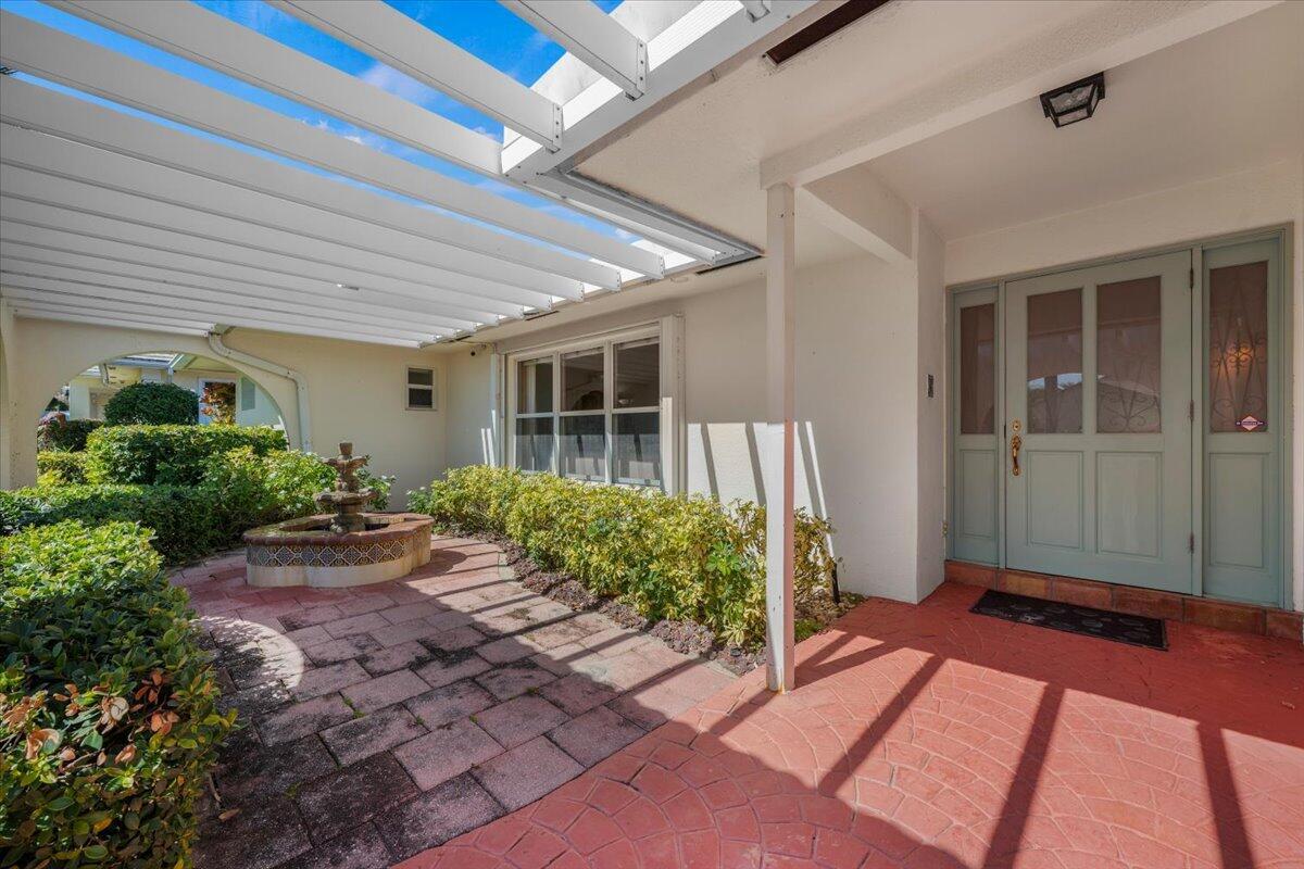 A patio with a fountain and pergola leads to a light blue front door — 103 Olympus Circle, Jupiter FL 33477, JUPITER, FL