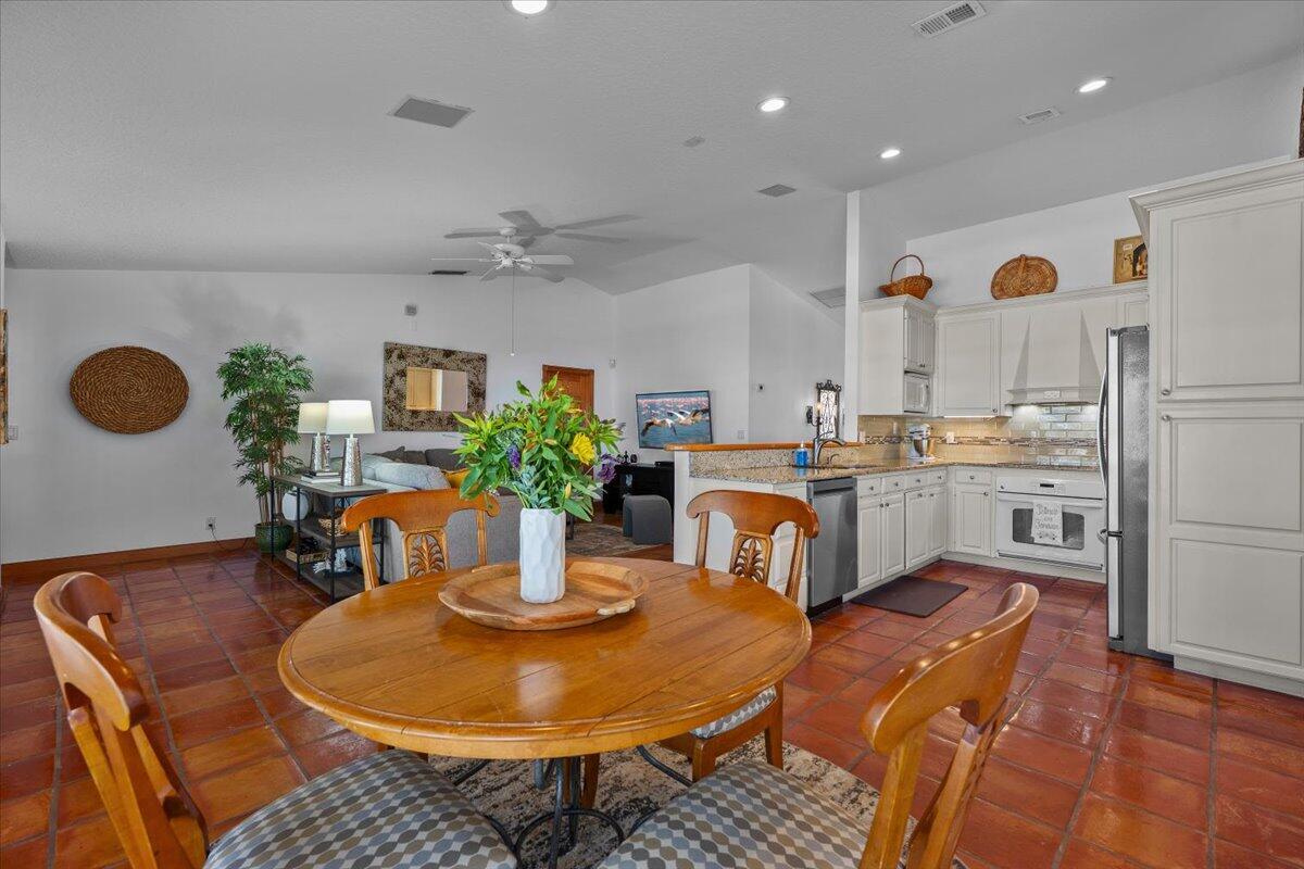 A dining area with a wooden table sits before an open kitchen with white cabinets — 103 Olympus Circle, Jupiter FL 33477, JUPITER, FL