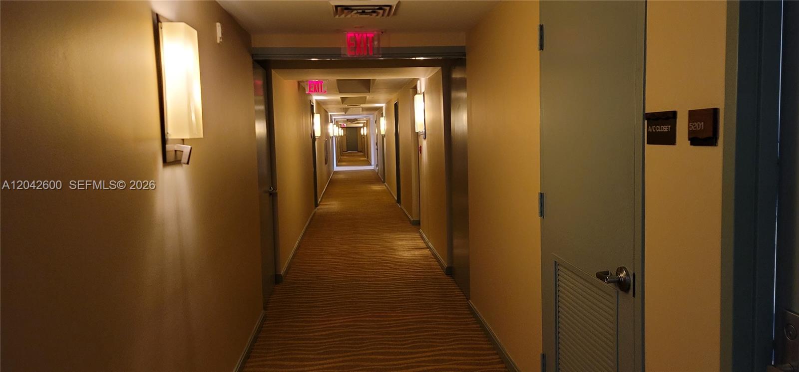 A long, carpeted apartment building hallway features beige walls, wall sconces, and unit doors — 50 Biscayne Blvd # 5202, Miami FL 33132, MIAMI, FL