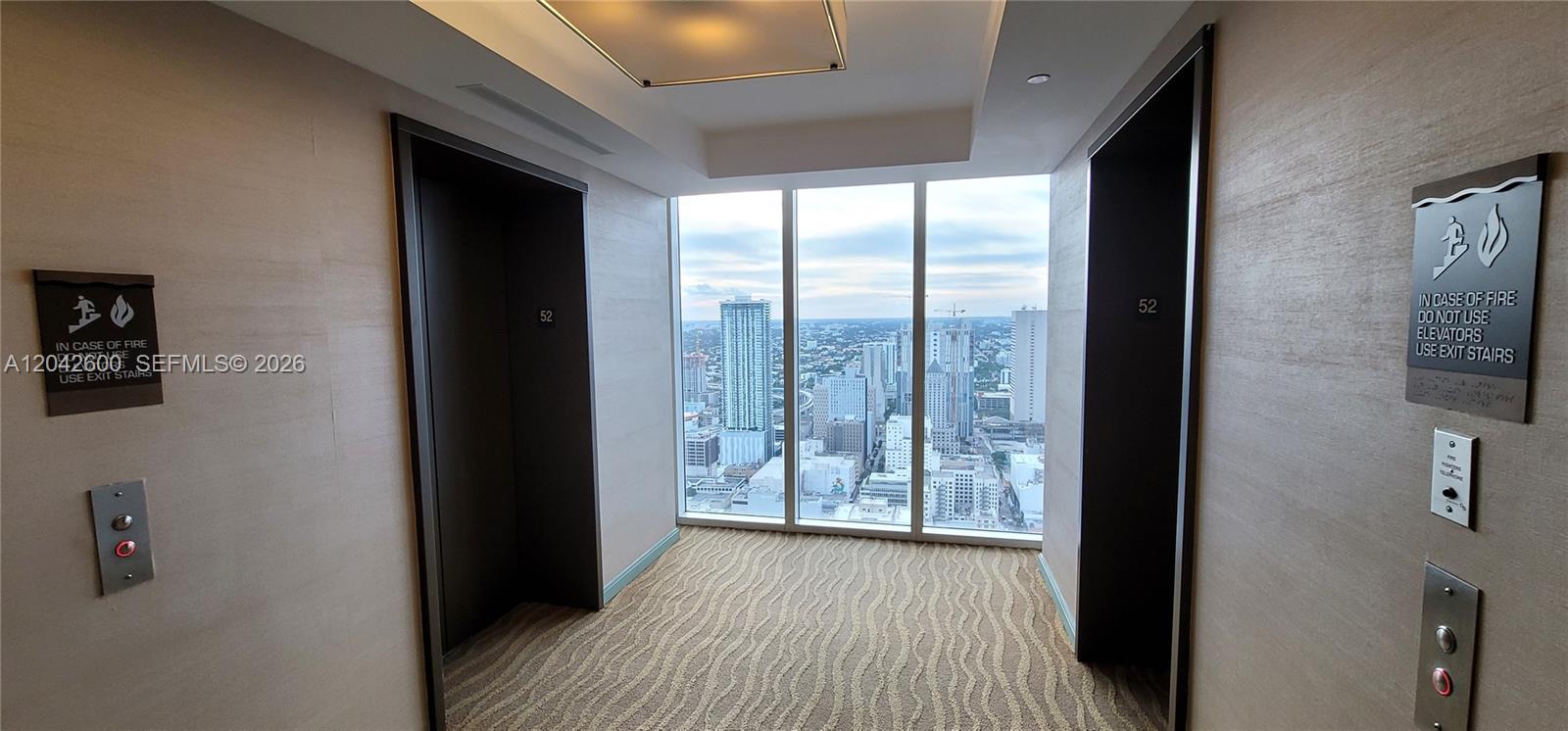 An elevator lobby on the 52nd floor features floor-to-ceiling windows overlooking a city skyline — 50 Biscayne Blvd # 5202, Miami FL 33132, MIAMI, FL
