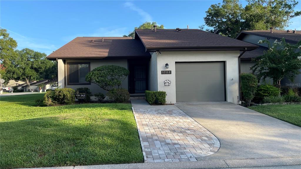 A single-story house features a brown shingled roof, stucco exterior, and a paved walkway — 1702 NE 38TH AVENUE, OCALA, FL