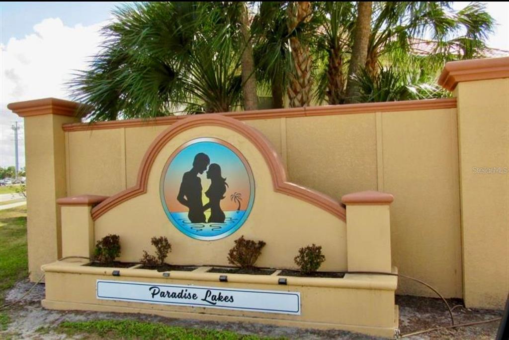 A tan stucco monument sign for Paradise Lakes features a circular logo with two silhouettes — 21103 PATIO VIEW COURT UNIT 3302, LUTZ, FL