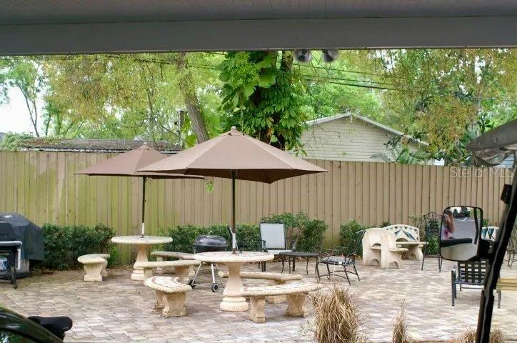 A paved patio features two dining tables with umbrellas, benches, and a grill near a fence — 21103 PATIO VIEW COURT UNIT 3302, LUTZ, FL