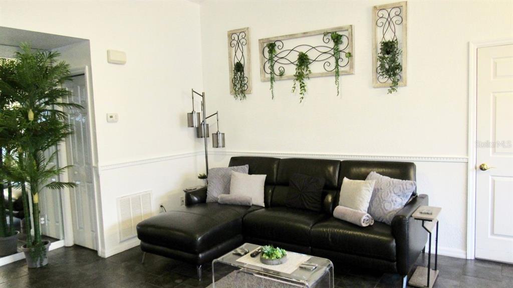A living room features a black leather sectional sofa, a glass coffee table, and wall decor — 21103 PATIO VIEW COURT UNIT 3302, LUTZ, FL