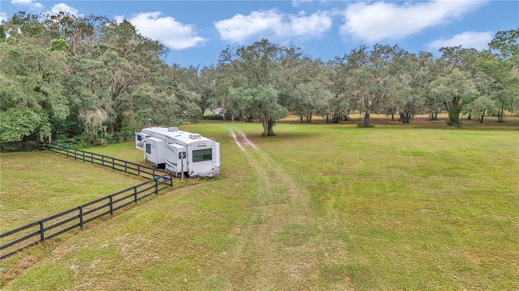 A white recreational vehicle is parked in a grassy field next to a black fence — 19597 SE 70TH LANE, MORRISTON, FL