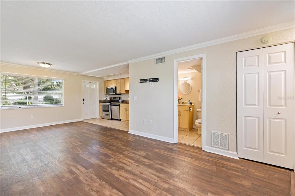 A living room with wood-look flooring leads to an open kitchen and a bathroom doorway — 960 HIGHLAND STREET UNIT A7, SARASOTA, FL