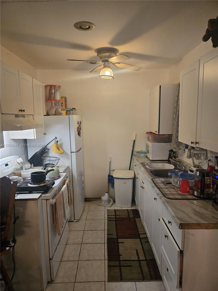 A galley kitchen features white cabinets, a white stove, a refrigerator, and tiled flooring — 10425 SW 146th Ter, Miami FL 33176, MIAMI, FL