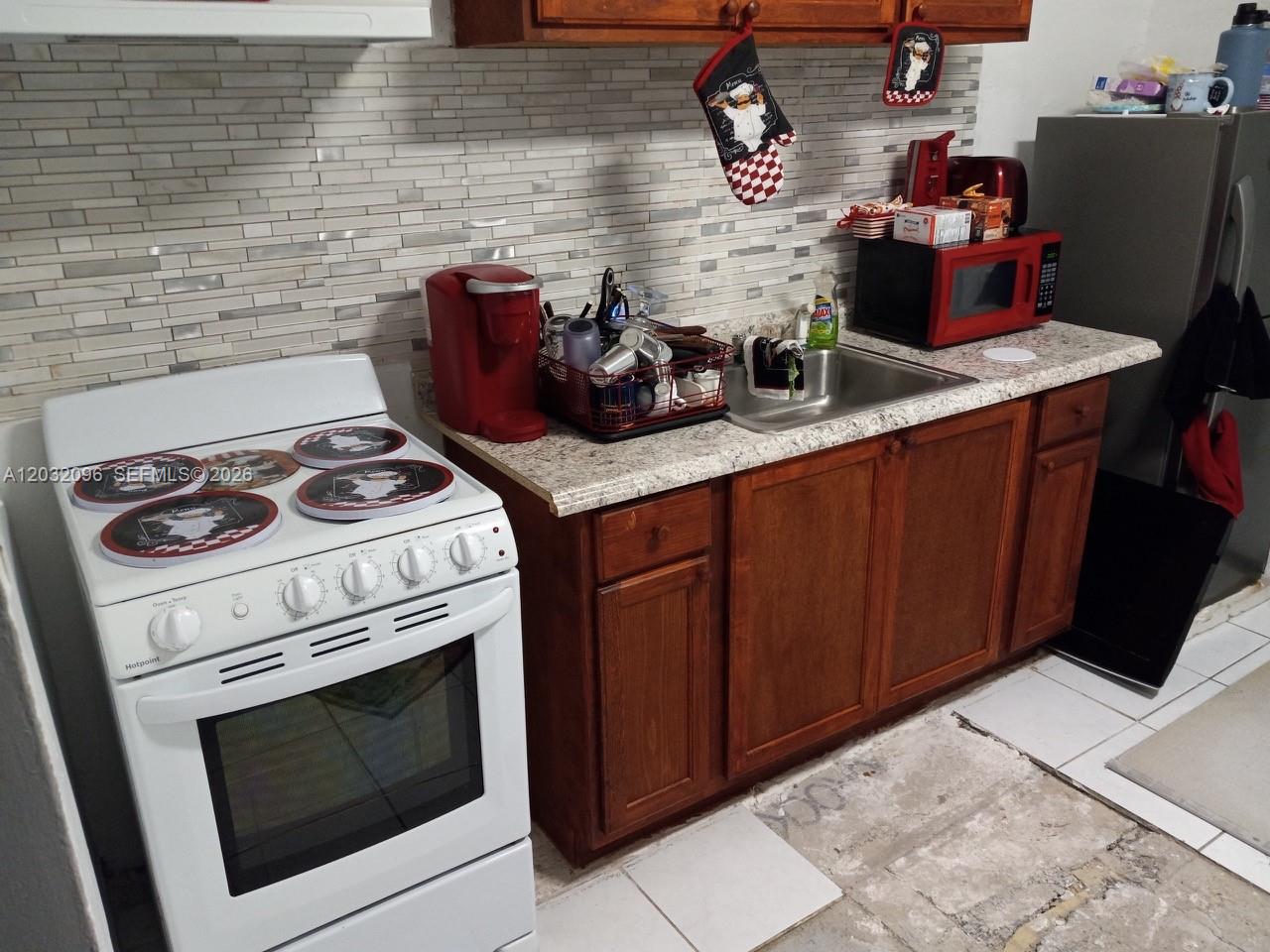 A kitchen features a white stove, wooden cabinets, a granite countertop, and a stainless sink — 1100 NW 57th St, Miami FL 33127, MIAMI, FL