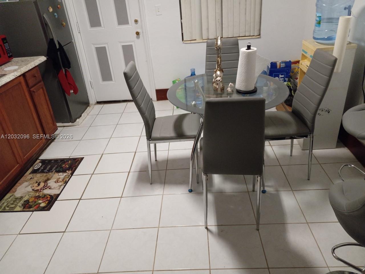 A dining area features a glass-topped table with four grey chairs on a tiled floor — 1100 NW 57th St, Miami FL 33127, MIAMI, FL