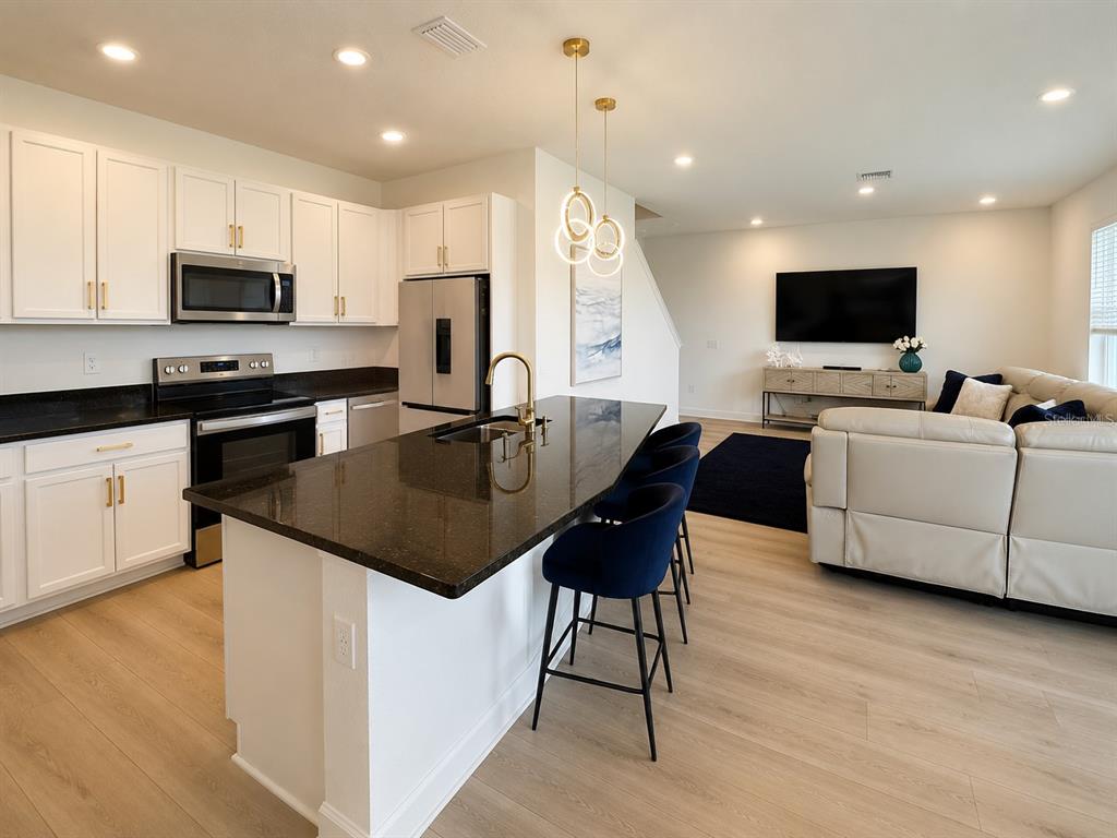 A kitchen with white cabinets and a dark island overlooks a living room with a television — 16522 BROOK ISLE WAY, CLERMONT, FL