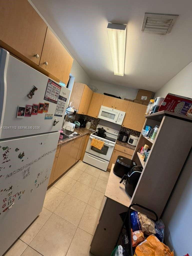 A galley-style kitchen features light wood cabinets, white appliances, and tile flooring — 2816 NW 15th St # 2R, Miami FL 33125, MIAMI, FL