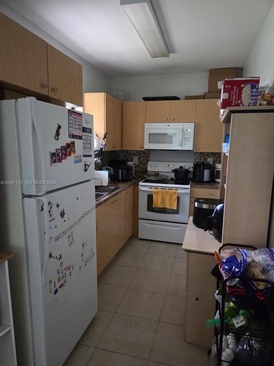 A kitchen features light wood cabinets, white appliances, a tiled backsplash, and beige floor tiles — 2816 NW 15th St # 2R, Miami FL 33125, MIAMI, FL