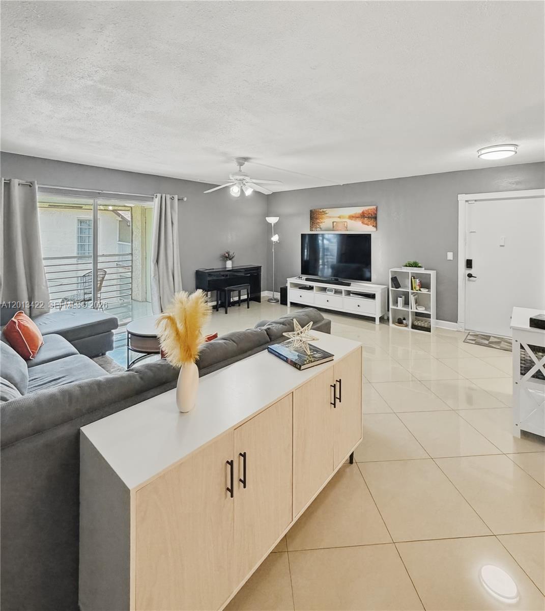 A living room features gray walls, tile flooring, a sectional sofa, and a sliding glass door — 406 N Laurel Dr # 207, Margate FL 33063, MARGATE, FL
