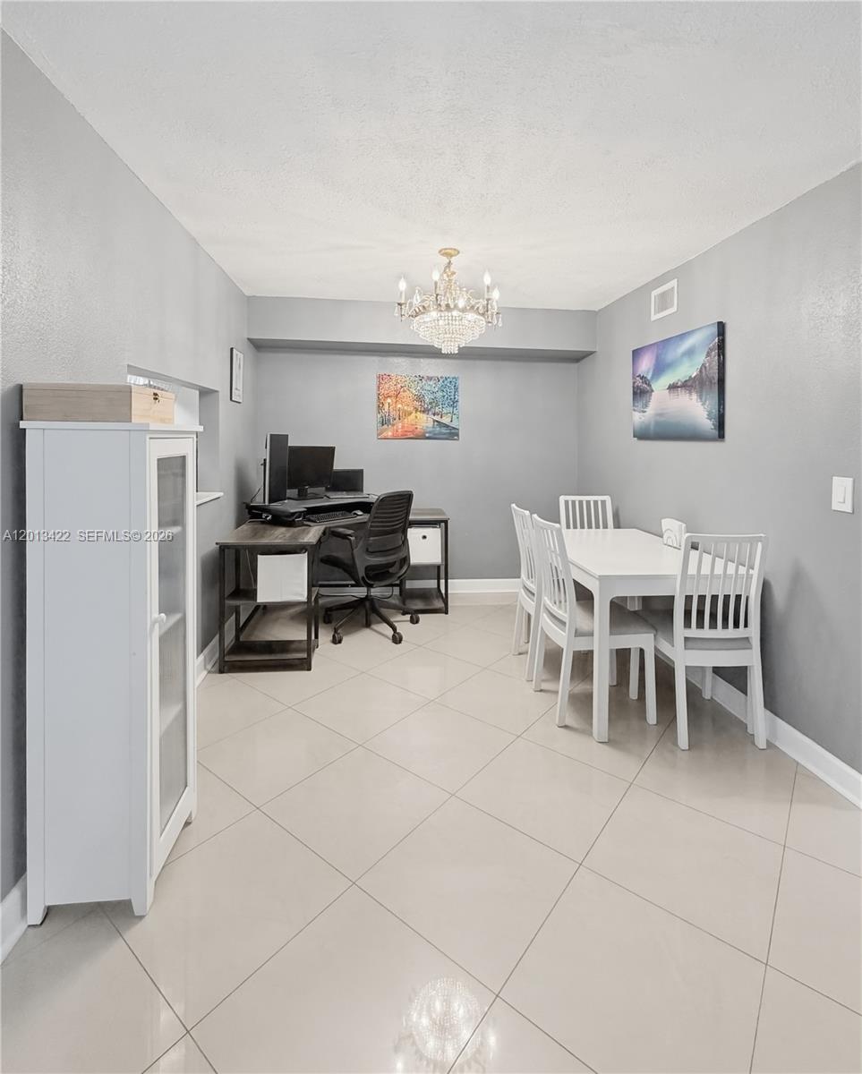 This dining room features light tile flooring, a crystal chandelier, and a built-in desk area — 406 N Laurel Dr # 207, Margate FL 33063, MARGATE, FL