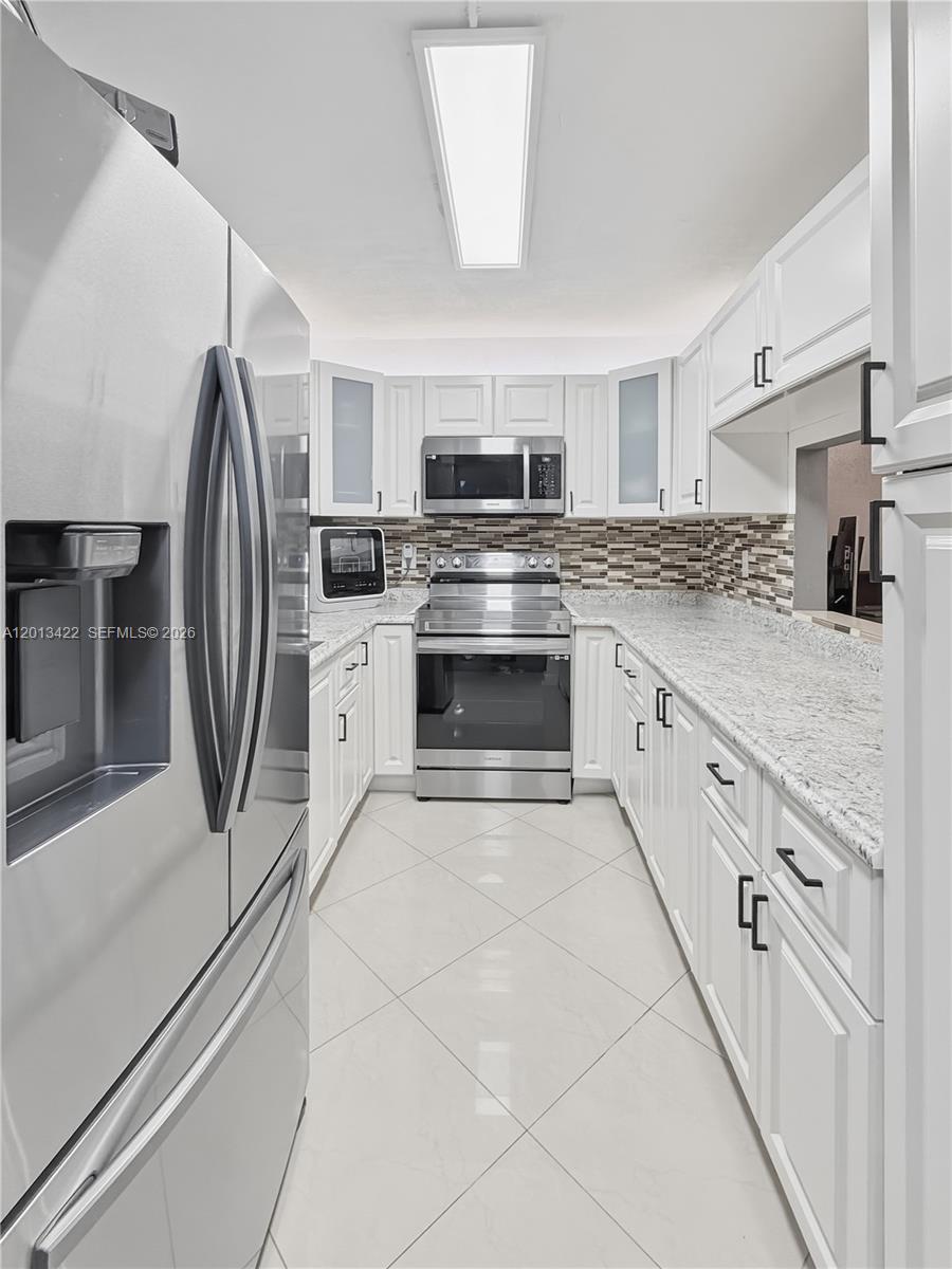 A galley kitchen features white cabinets, stainless steel appliances, and granite countertops — 406 N Laurel Dr # 207, Margate FL 33063, MARGATE, FL