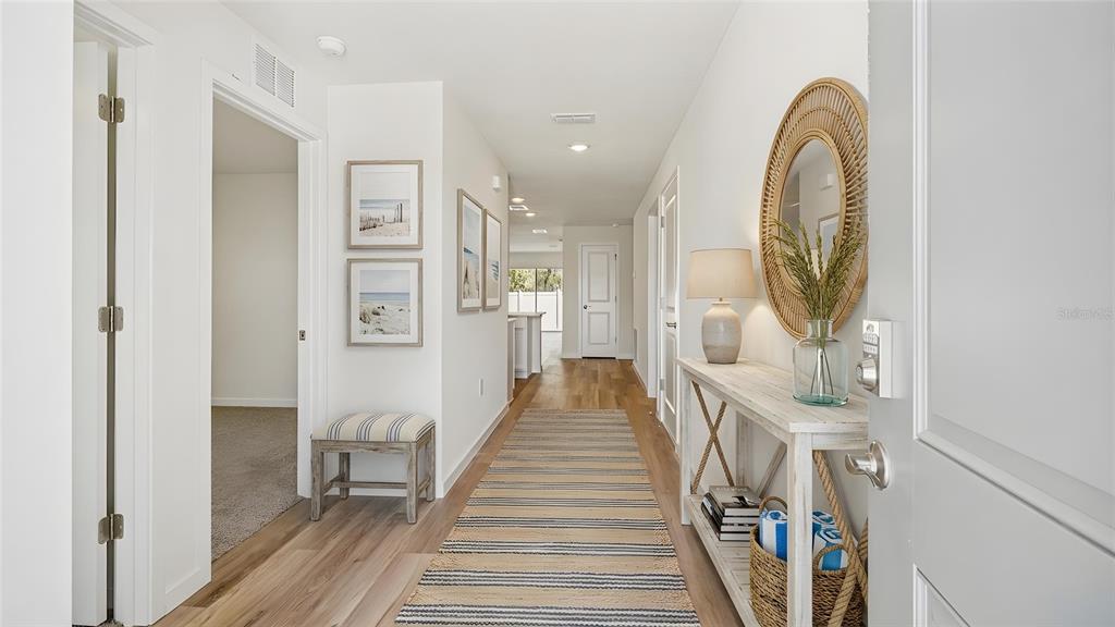 A bright entryway features light wood flooring, a console table, a striped runner, and wall art — 10128 SE 158TH LANE, SUMMERFIELD, FL