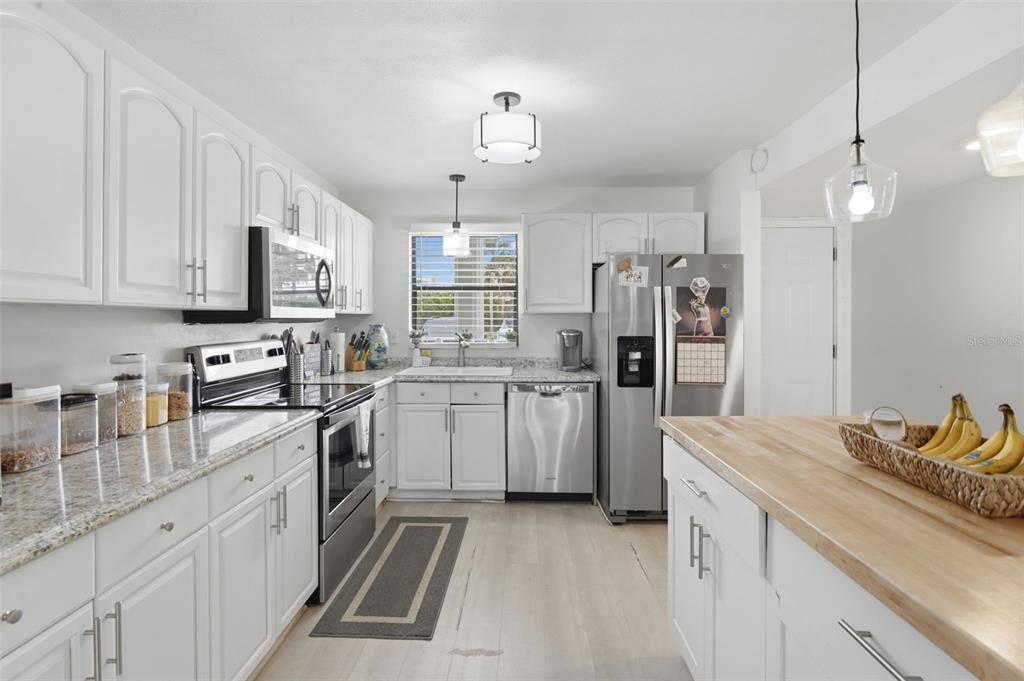 A kitchen features white cabinets, granite countertops, stainless steel appliances, and a wooden island — 2100 N PENINSULA AVENUE UNIT 1130, NEW SMYRNA BEACH, FL