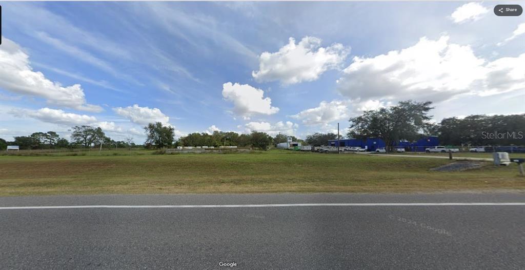 A wide, grassy vacant lot sits alongside a paved road under a partly cloudy sky — N/A, POLK CITY, FL
