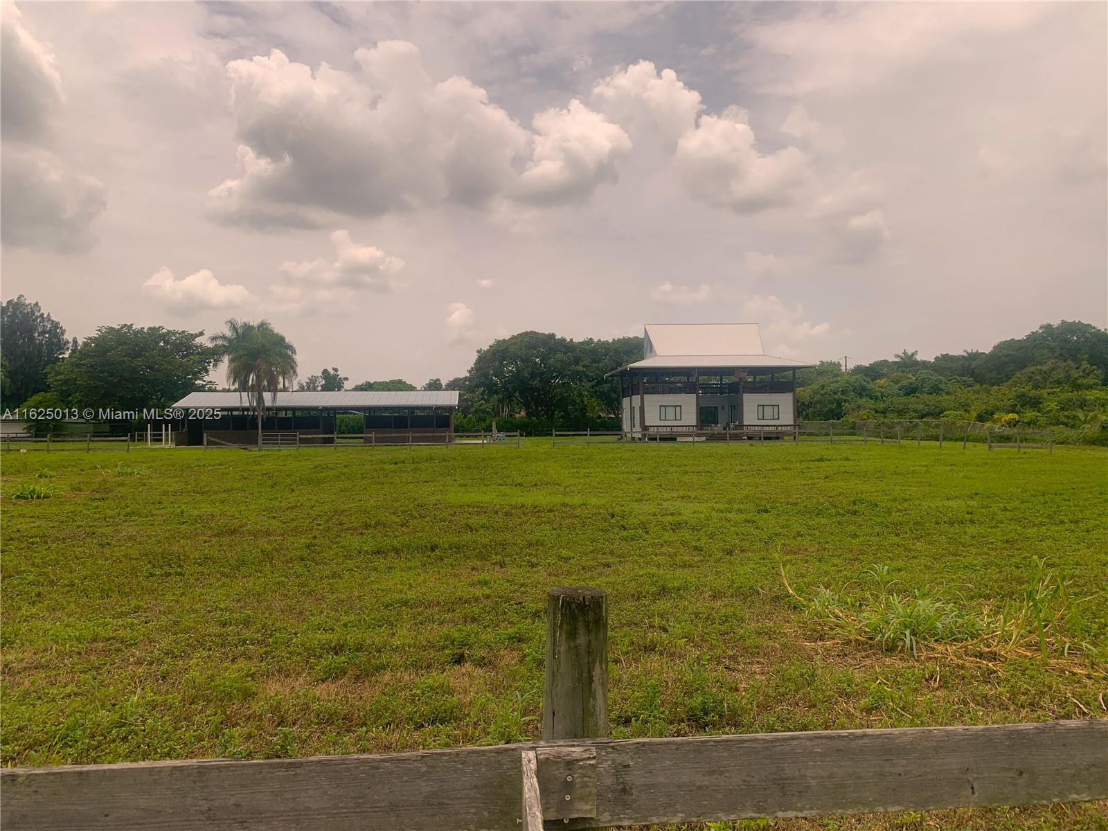 A grassy field features a wooden fence, a stable, and a two-story house under clouds — 22750 SW 154th ave, Miami FL 33170, MIAMI, FL