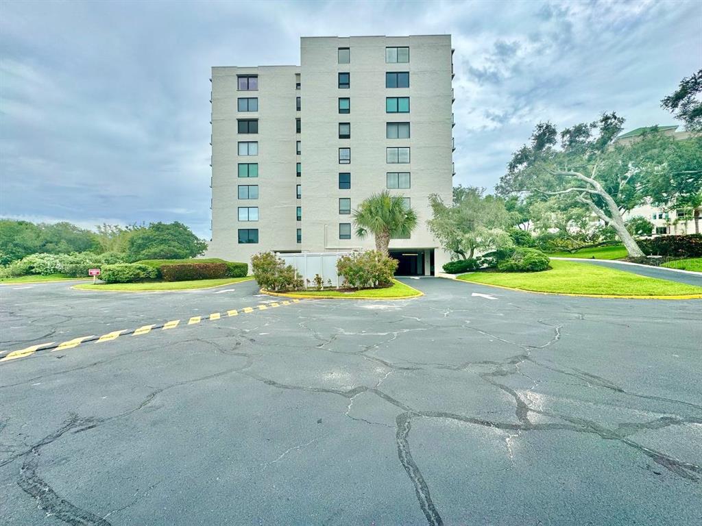A multi-story beige apartment building stands behind a paved parking lot with mature trees — 220 BELLEVIEW BOULEVARD UNIT 311, CLEARWATER, FL