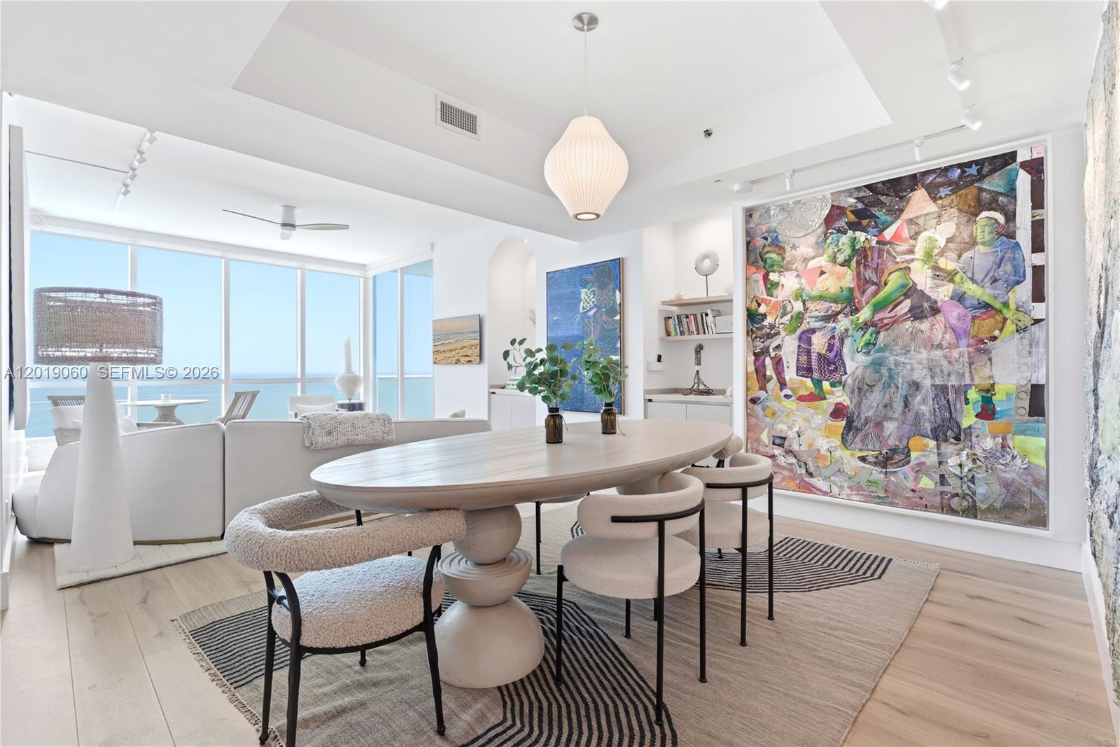 A modern dining room features an oval wooden table, textured chairs, and large abstract wall art — 100 S Pointe Dr # 1807, Miami Beach FL 33139, MIAMI BEACH, FL