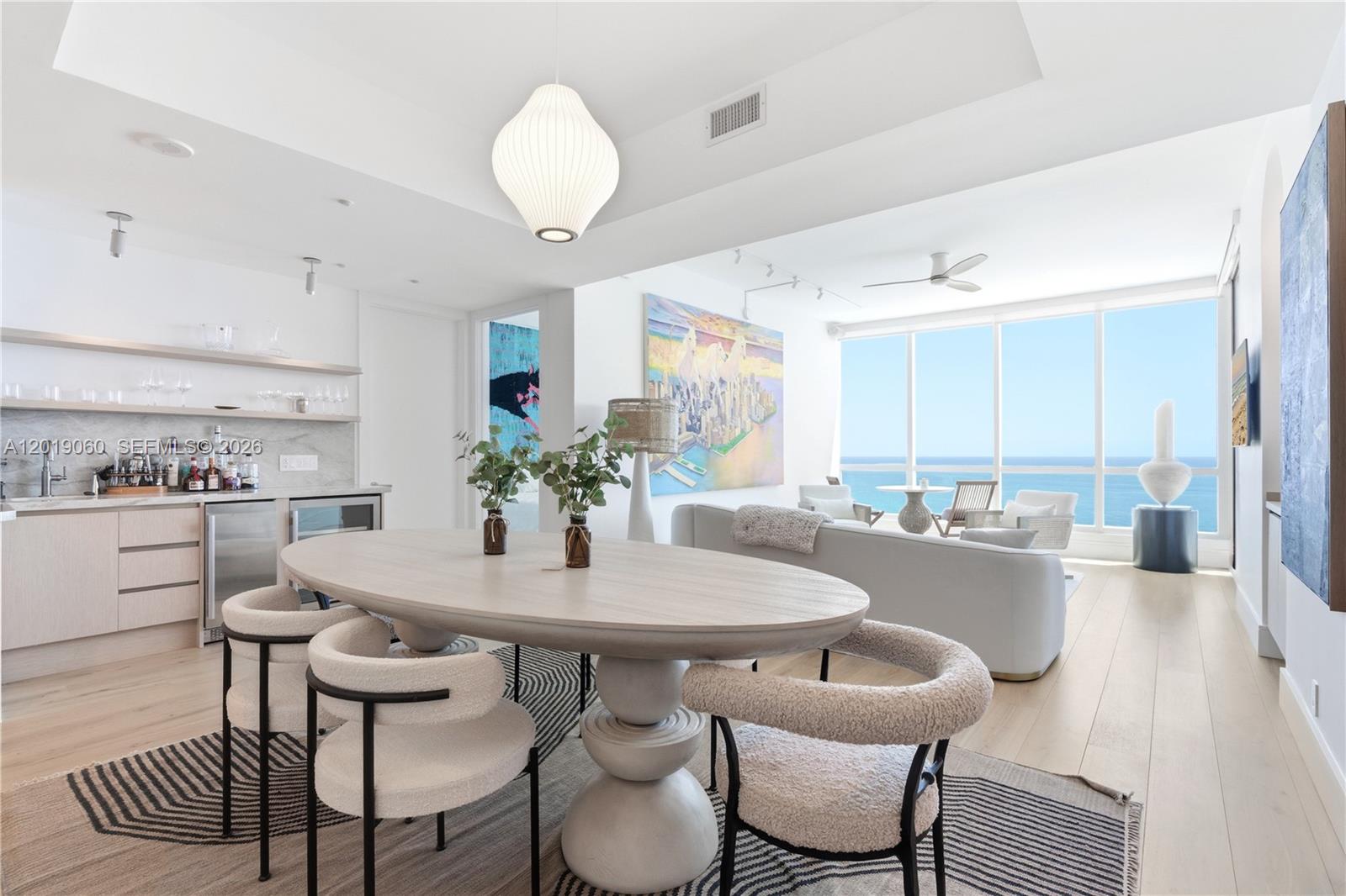 A dining area with an oval table and textured chairs overlooks the ocean through windows — 100 S Pointe Dr # 1807, Miami Beach FL 33139, MIAMI BEACH, FL