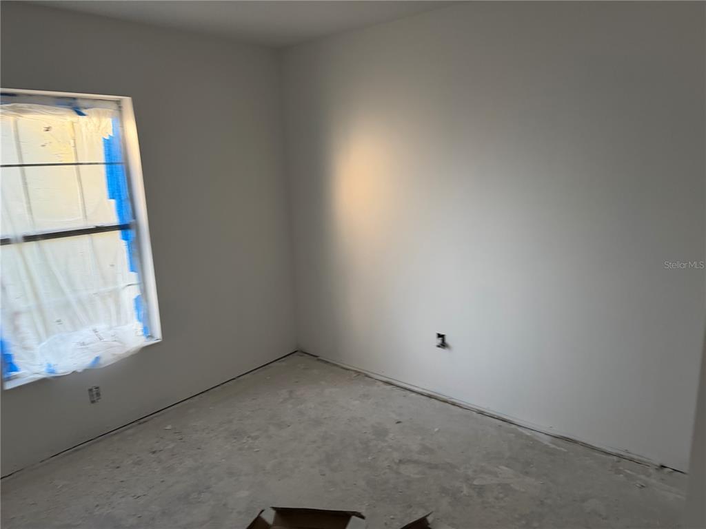 An unfinished bedroom features white walls, a window covered in plastic, and a concrete floor — 5907 NW 64TH STREET, OCALA, FL