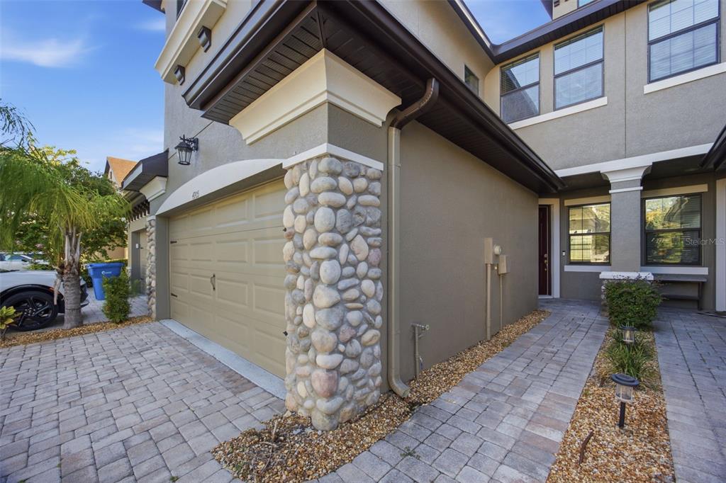 A stone-accented corner pillar stands beside a garage door and a paved walkway — 4905 WANDERING WAY, WESLEY CHAPEL, FL