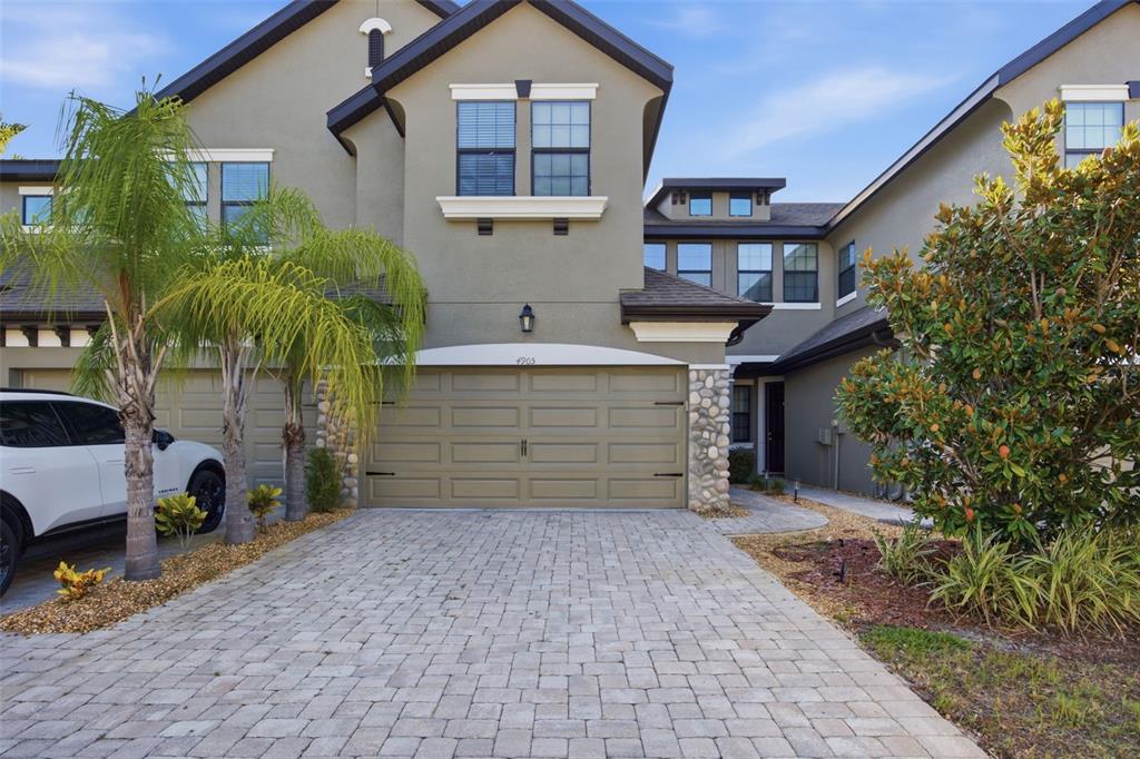 A two-story townhouse with a paved driveway, a two-car garage, and palm trees — 4905 WANDERING WAY, WESLEY CHAPEL, FL