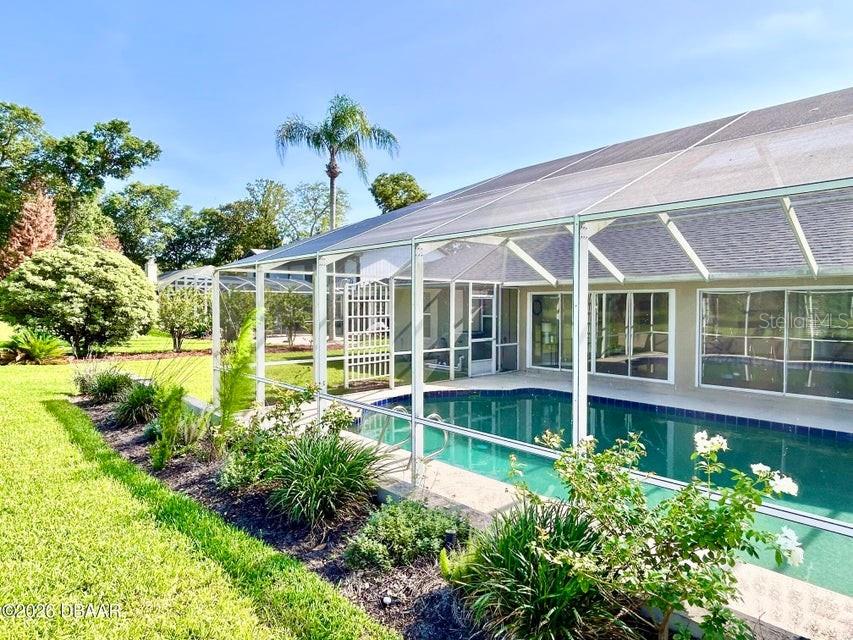 A screened-in swimming pool sits adjacent to a house with a large backyard — 123 RIO PINAR DRIVE, ORMOND BEACH, FL