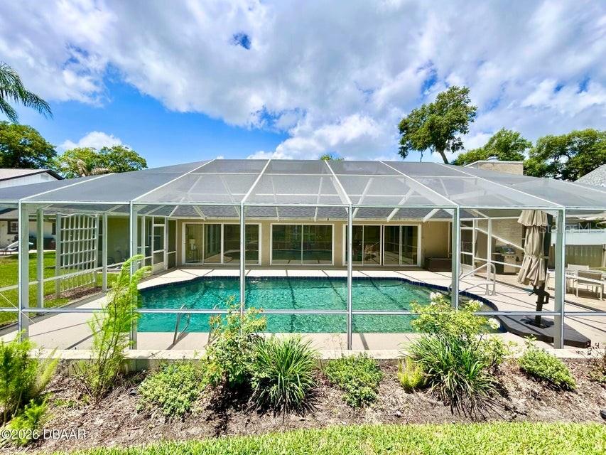 A screened-in swimming pool sits behind a house with large glass sliding doors — 123 RIO PINAR DRIVE, ORMOND BEACH, FL