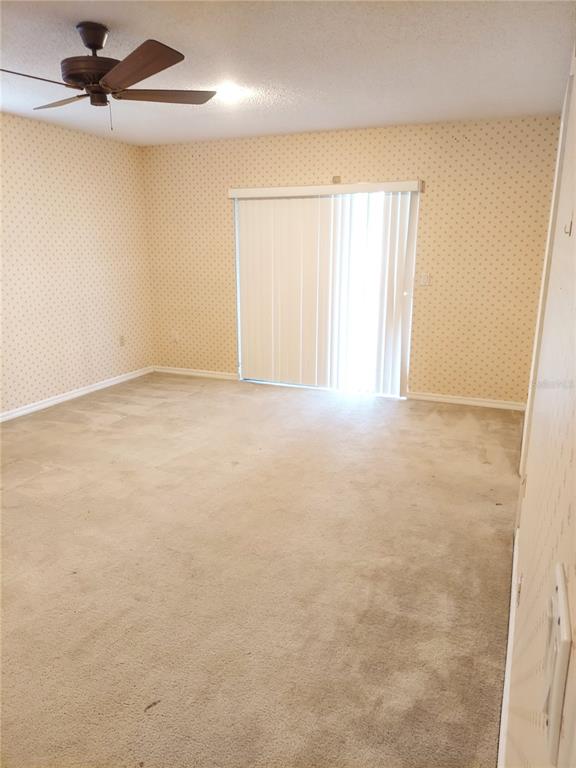 A bedroom with beige patterned wallpaper, tan carpeting, a ceiling fan, and sliding glass doors — 8139 LAUREL TREE DRIVE, ORLANDO, FL
