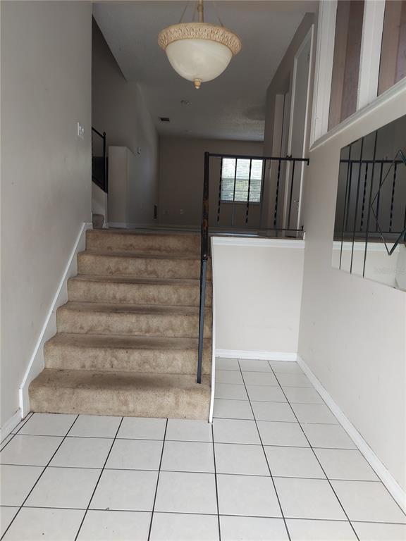 An entryway features a tiled floor, a carpeted staircase, and a hanging light fixture — 8139 LAUREL TREE DRIVE, ORLANDO, FL