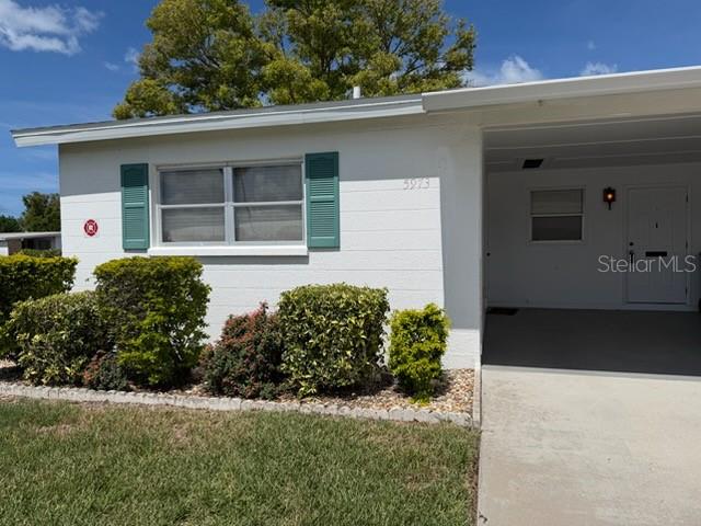 A white, single-story house with a carport and green shutters sits on a grassy lawn — 5973 HIBISCUS DRIVE, BRADENTON, FL
