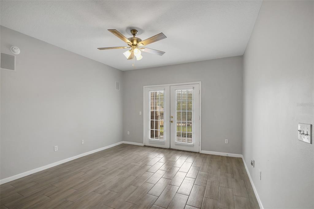 A room with light gray walls, wood-look tile flooring, a ceiling fan, and glass-paned double doors — 14316 FREDRICKSBURG DRIVE UNIT 518, ORLANDO, FL