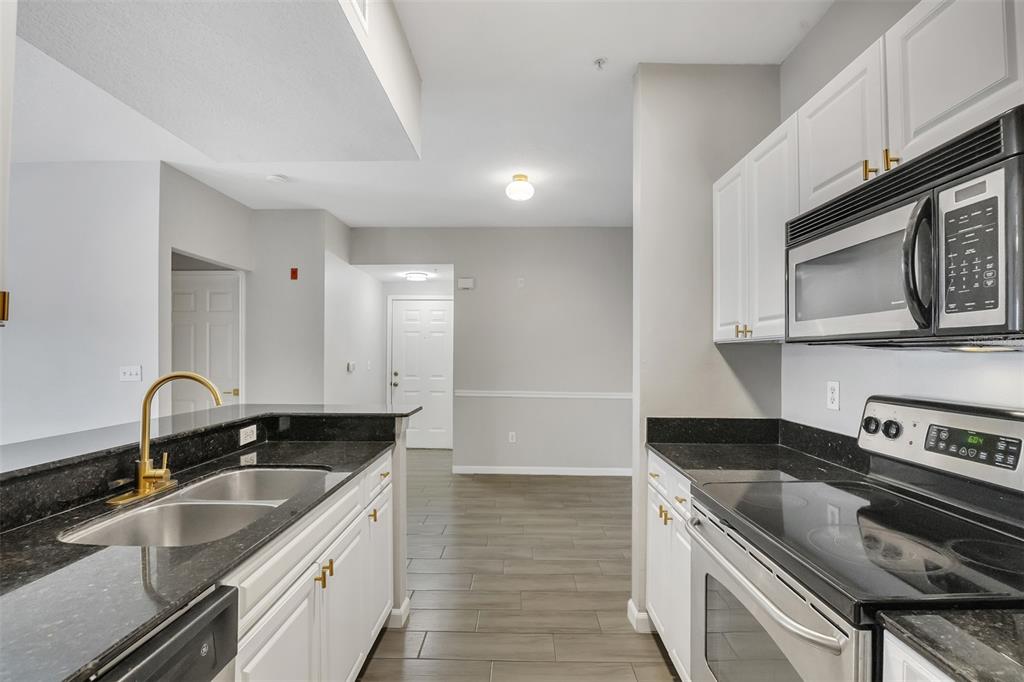 A galley kitchen features white cabinets, black countertops, stainless steel appliances, and wood-look tile flooring — 14316 FREDRICKSBURG DRIVE UNIT 518, ORLANDO, FL