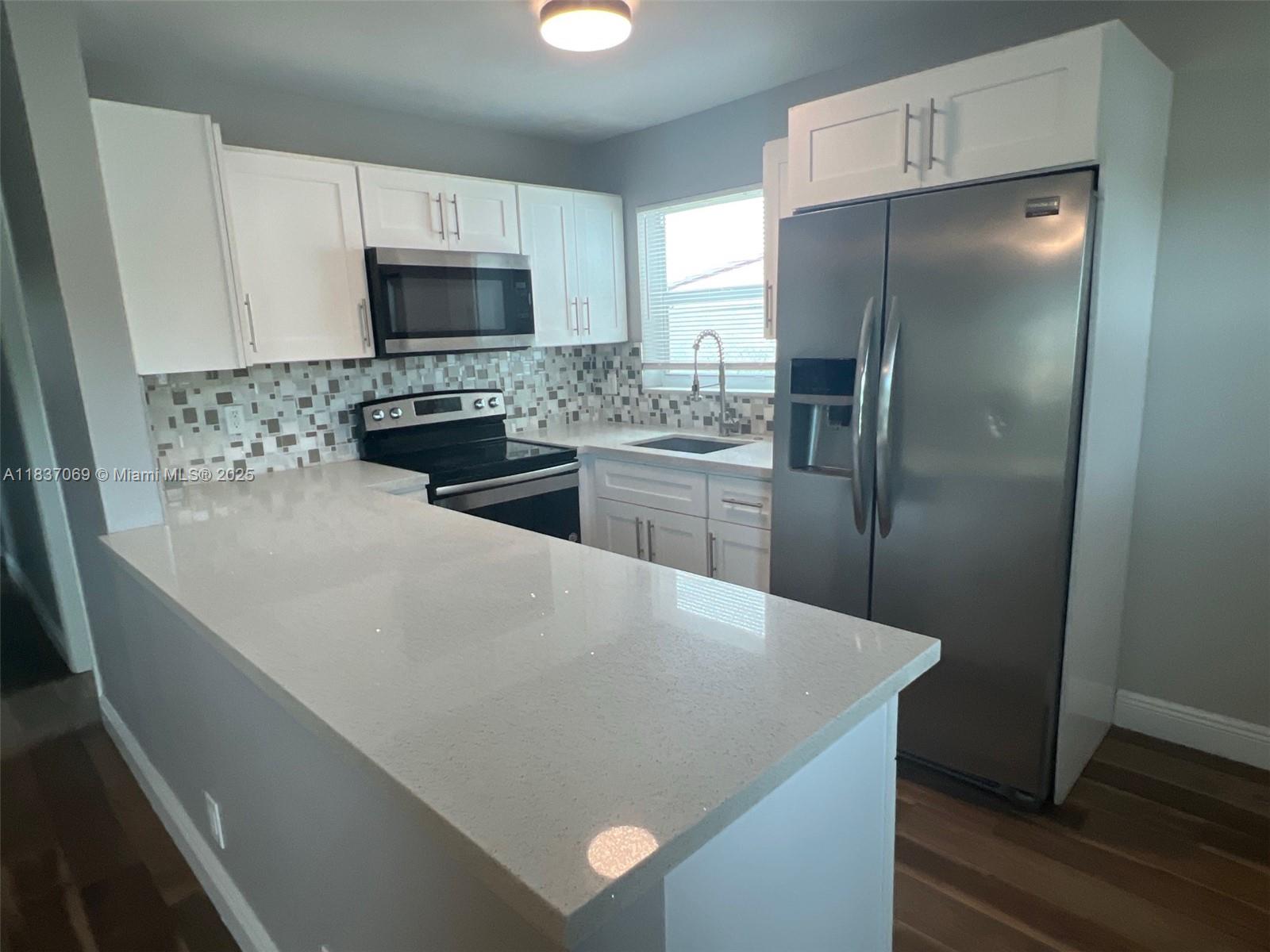 A kitchen features white cabinets, stainless steel appliances, a tiled backsplash, and a quartz countertop — 2569 NW 61st Ave, Margate FL 33063, MARGATE, FL
