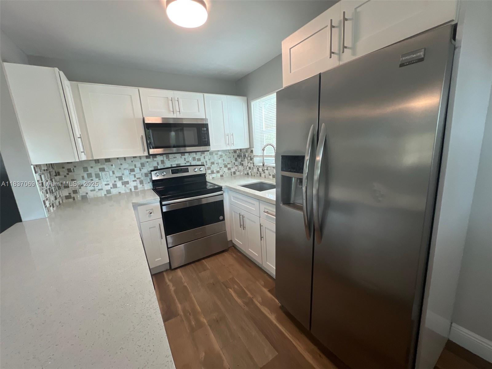 A modern kitchen features white cabinets, stainless steel appliances, a mosaic backsplash, and wood flooring — 2569 NW 61st Ave, Margate FL 33063, MARGATE, FL