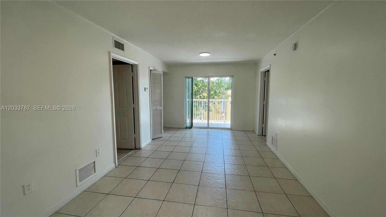 An empty room with tiled floors, white walls, two doorways, and a sliding glass balcony door — 2475 NW 16th St Rd # 309, Miami FL 33125, MIAMI, FL