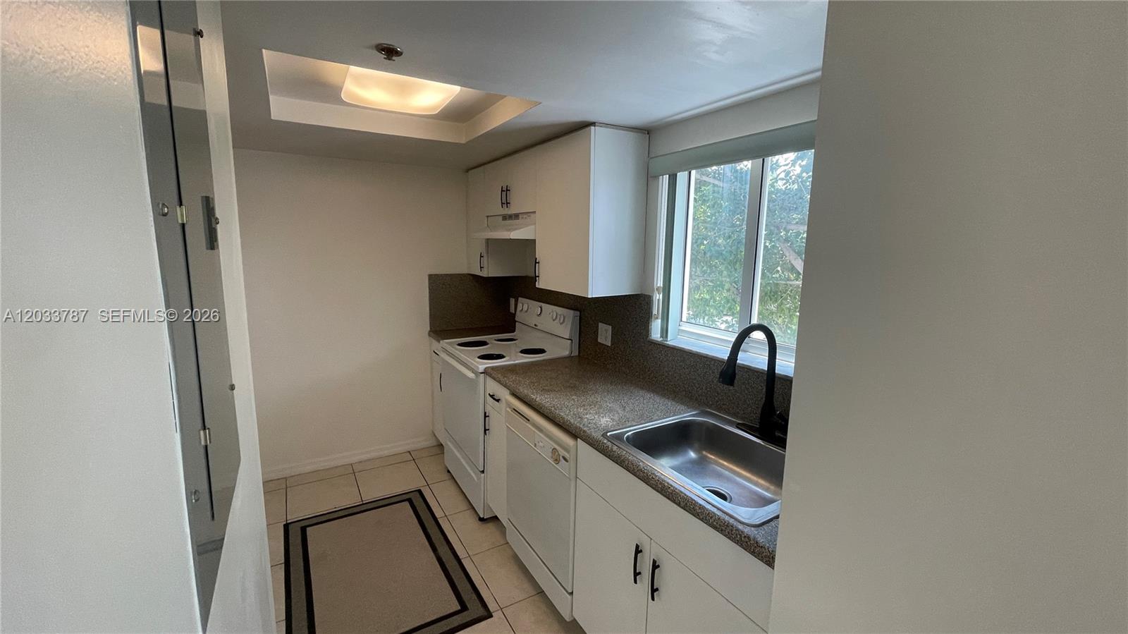 A small kitchen features white cabinets, a stainless steel sink, and white appliances — 2475 NW 16th St Rd # 309, Miami FL 33125, MIAMI, FL