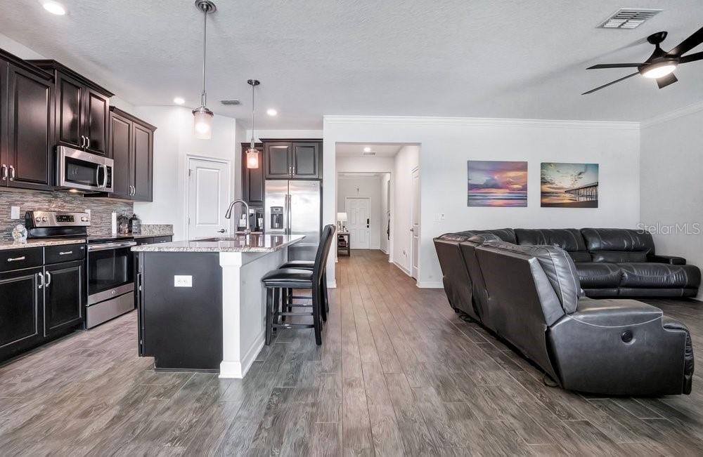A kitchen with dark cabinets and a breakfast bar opens into a living room area — 14192 GOLD BRIDGE DRIVE, ORLANDO, FL