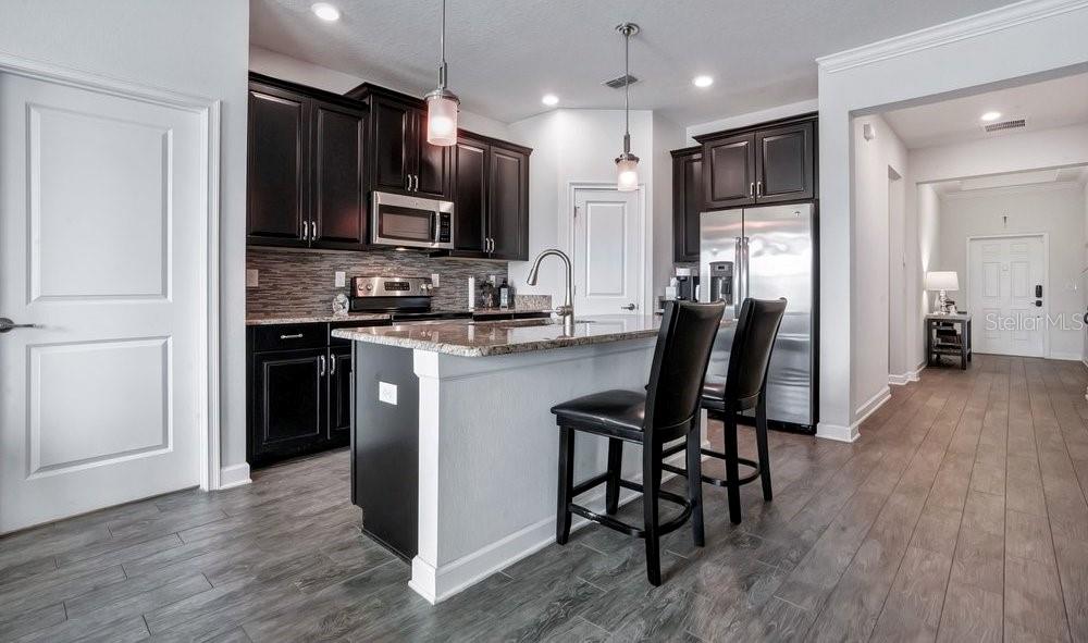 A kitchen with dark cabinets, stainless steel appliances, a granite island, and wood-look tile flooring — 14192 GOLD BRIDGE DRIVE, ORLANDO, FL