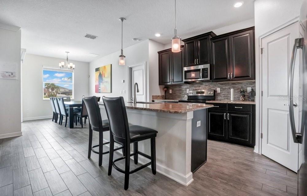 A kitchen with dark cabinets, granite countertops, and a breakfast bar overlooking a dining area — 14192 GOLD BRIDGE DRIVE, ORLANDO, FL