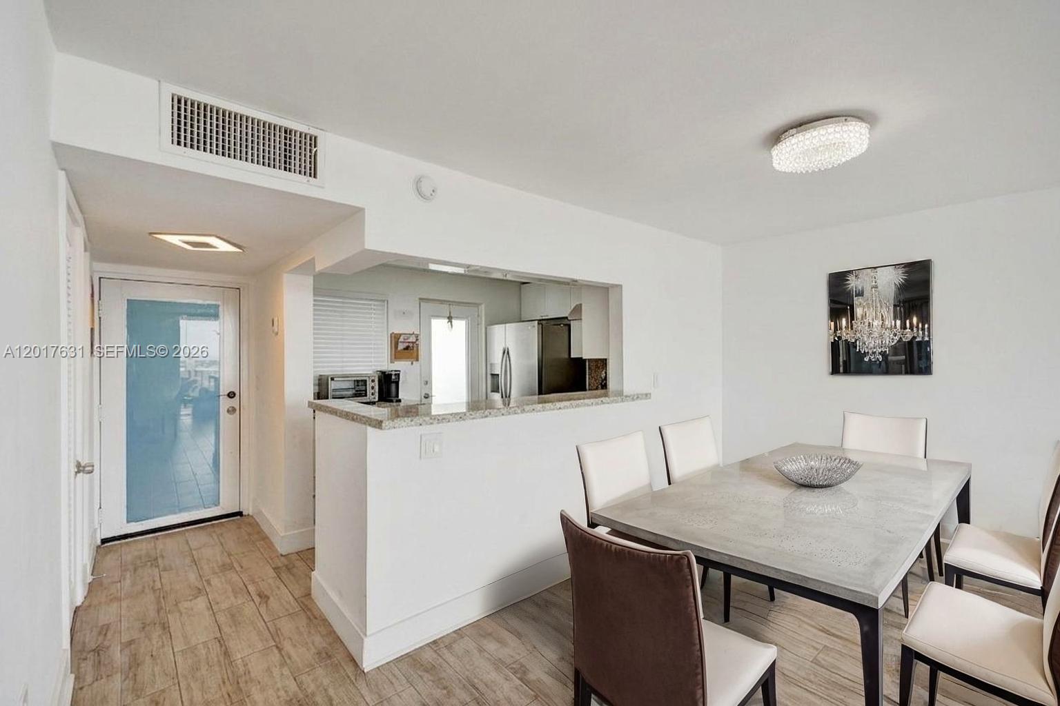 A dining area features a stone-topped table, white chairs, and a pass-through kitchen counter — 7850 Byron Ave # 702, Miami Beach FL 33141, MIAMI BEACH, FL