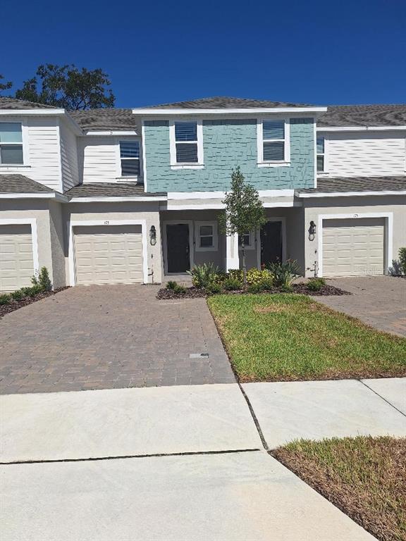 A two-story townhouse exterior with beige siding, a teal shingled accent wall, and two garages — 173 RIVER FRONT WAY, EDGEWATER, FL
