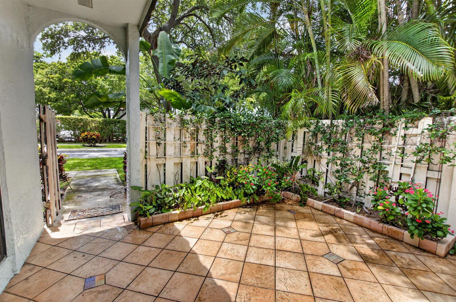 A tiled patio features a white lattice fence covered in vines and lush tropical landscaping — 22270 Pineapple Walk Drive, Boca Raton FL 33433, BOCA RATON, FL