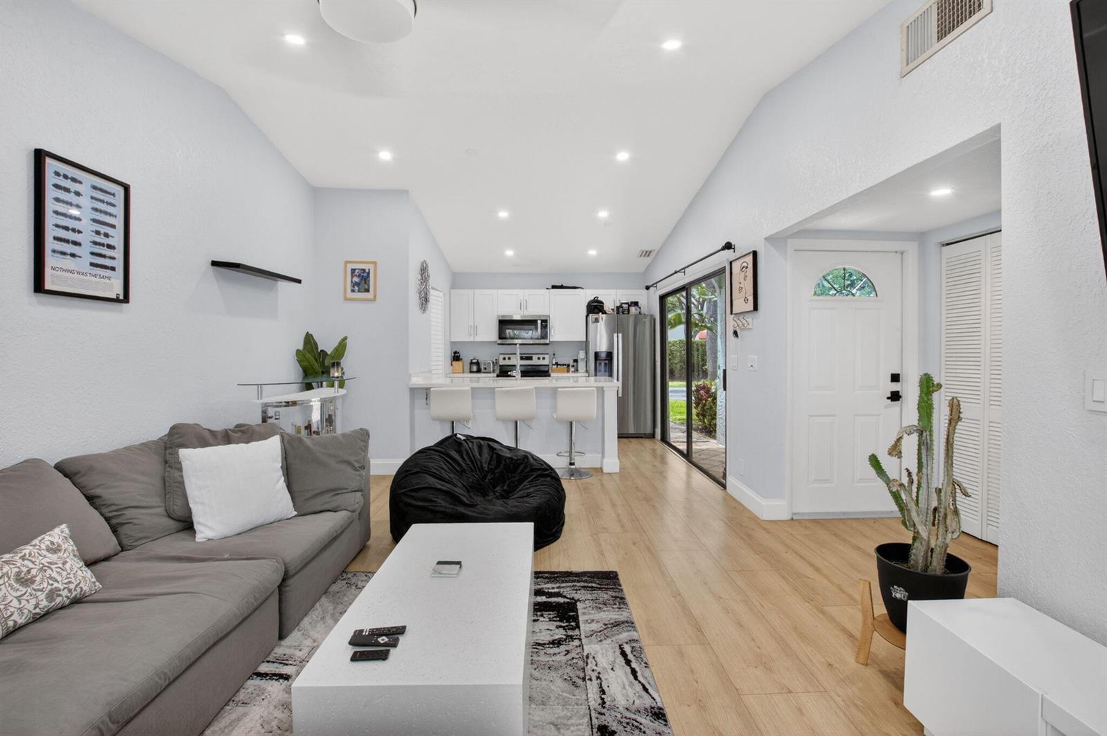 A living room with a grey sofa, beanbag chair, and open kitchen with white cabinets — 22270 Pineapple Walk Drive, Boca Raton FL 33433, BOCA RATON, FL