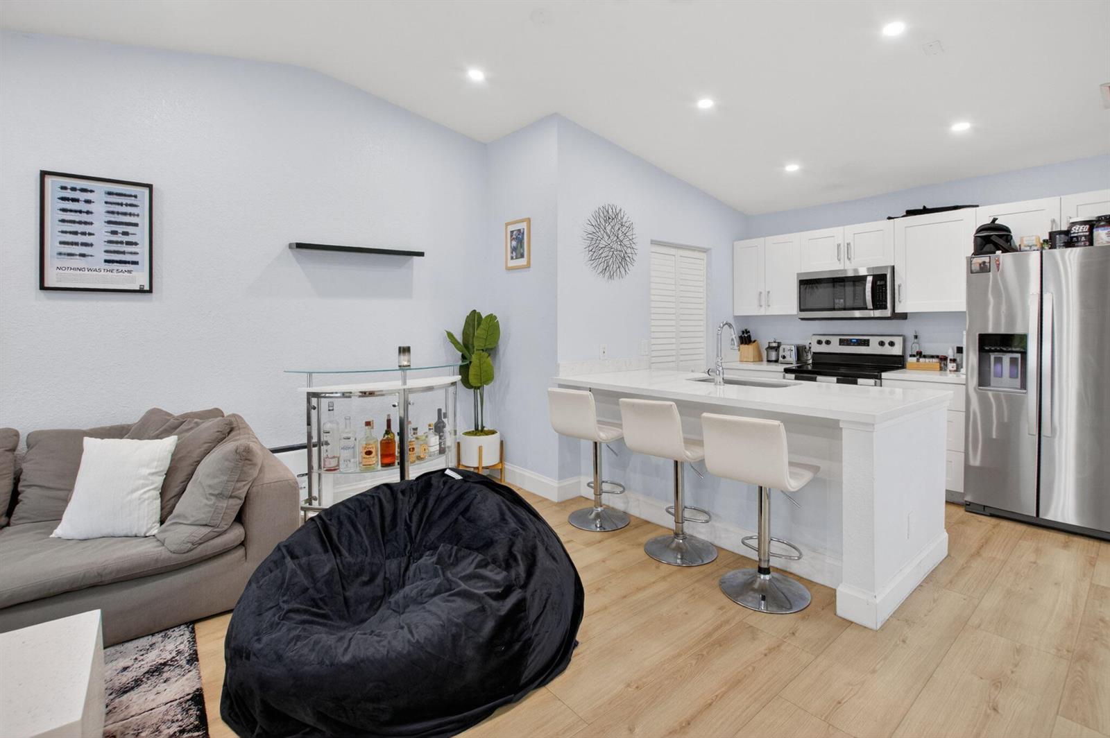 A kitchen with white cabinets and an island opens into a living area with seating — 22270 Pineapple Walk Drive, Boca Raton FL 33433, BOCA RATON, FL