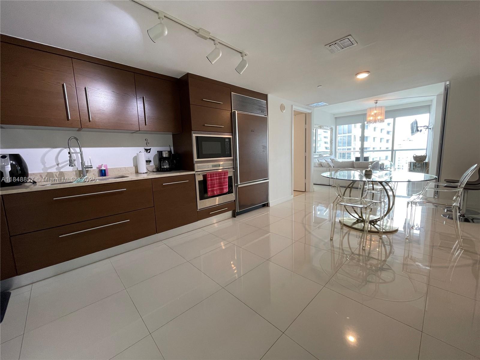 A modern kitchen with dark wood cabinetry and white tile floors opens to a dining area — 485 Brickell Ave # 3711, Miami FL 33131, MIAMI, FL